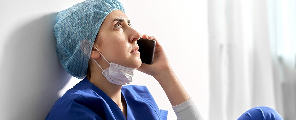 Traurige und müde junge Ärztin oder Krankenschwester, die auf dem Boden sitzt und ein Handy ans Ohr hält Traurige und müde junge Ärztin oder Krankenschwester, die auf dem Boden sitzt und ein Handy ans Ohr hält
